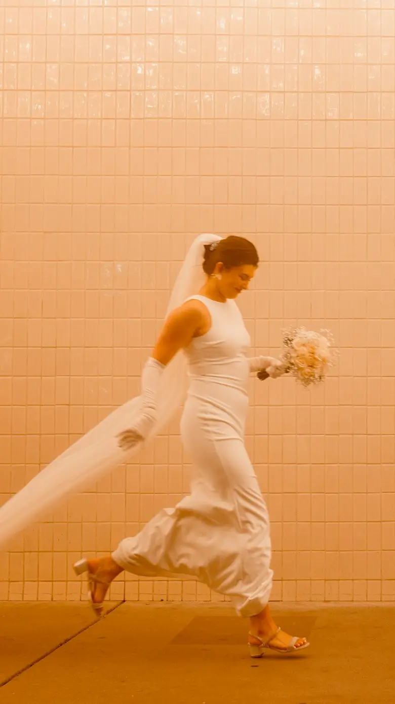 A bride in a long white dress and veil walks past a warm peach tiled wall in Las Vegas, bouquet in hand
