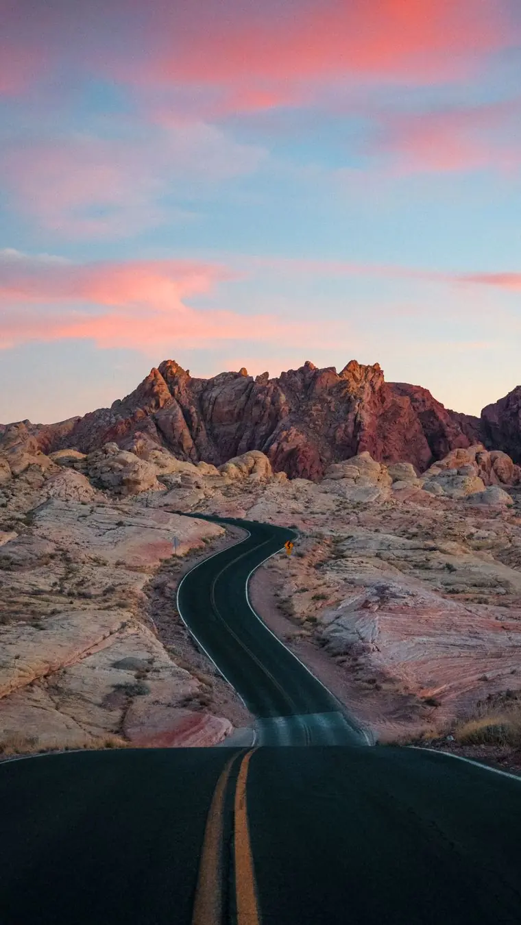 A road curling through cream and pink sandstone under pink and peach dusk cloud