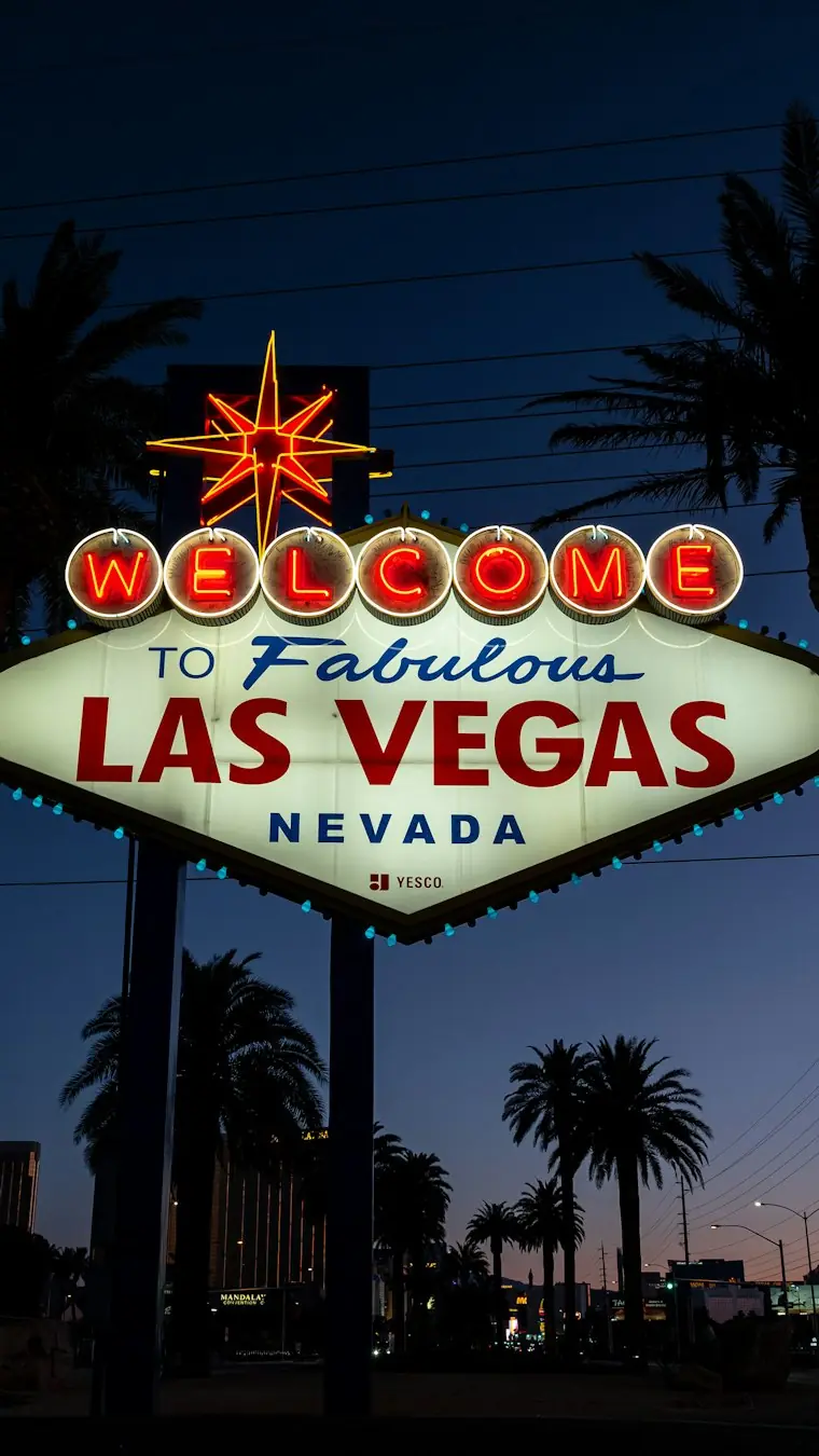 The Welcome to Fabulous Las Vegas sign lit up just after sunset, tall palms against a deep blue sky